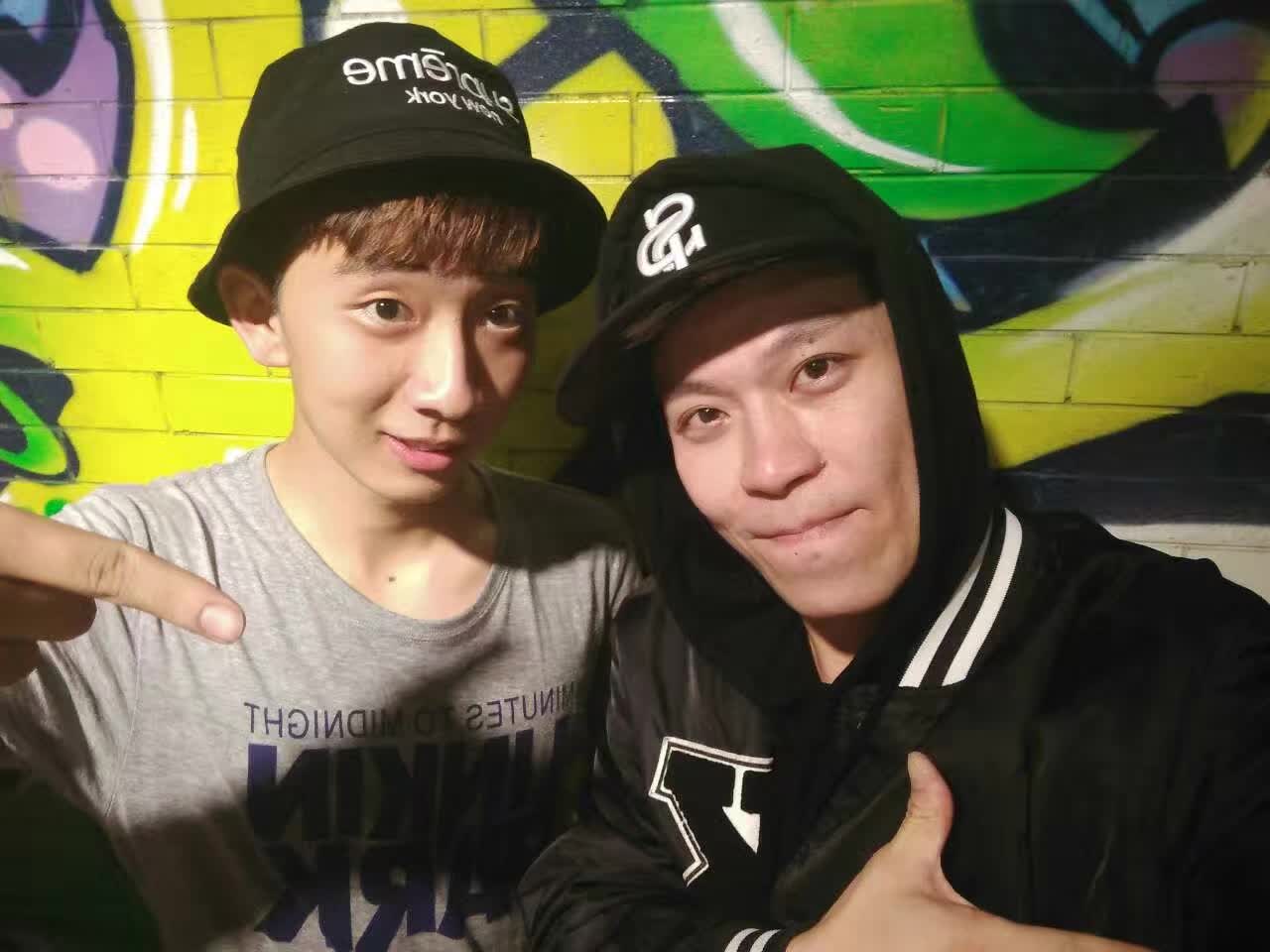Two people posing together in front of a colorful graffiti wall.
