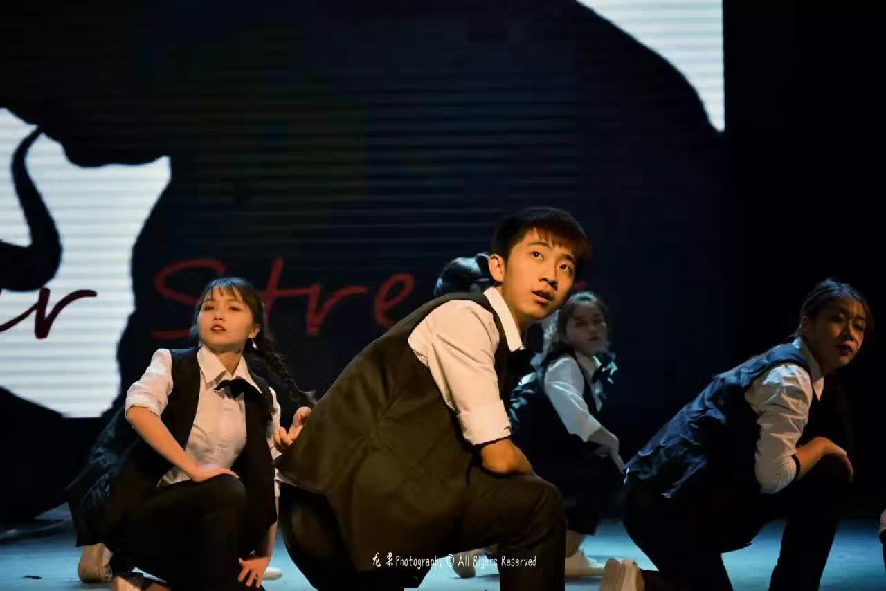 Dancers performing on stage in white shirts and dark vests.