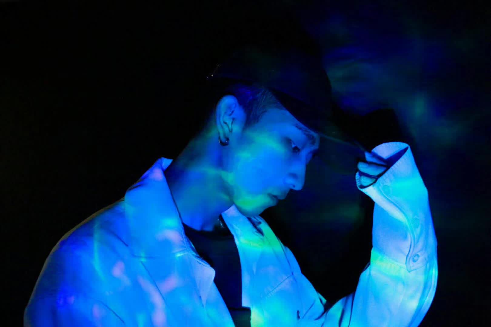 A person in a cap and light-colored jacket under blue lighting.