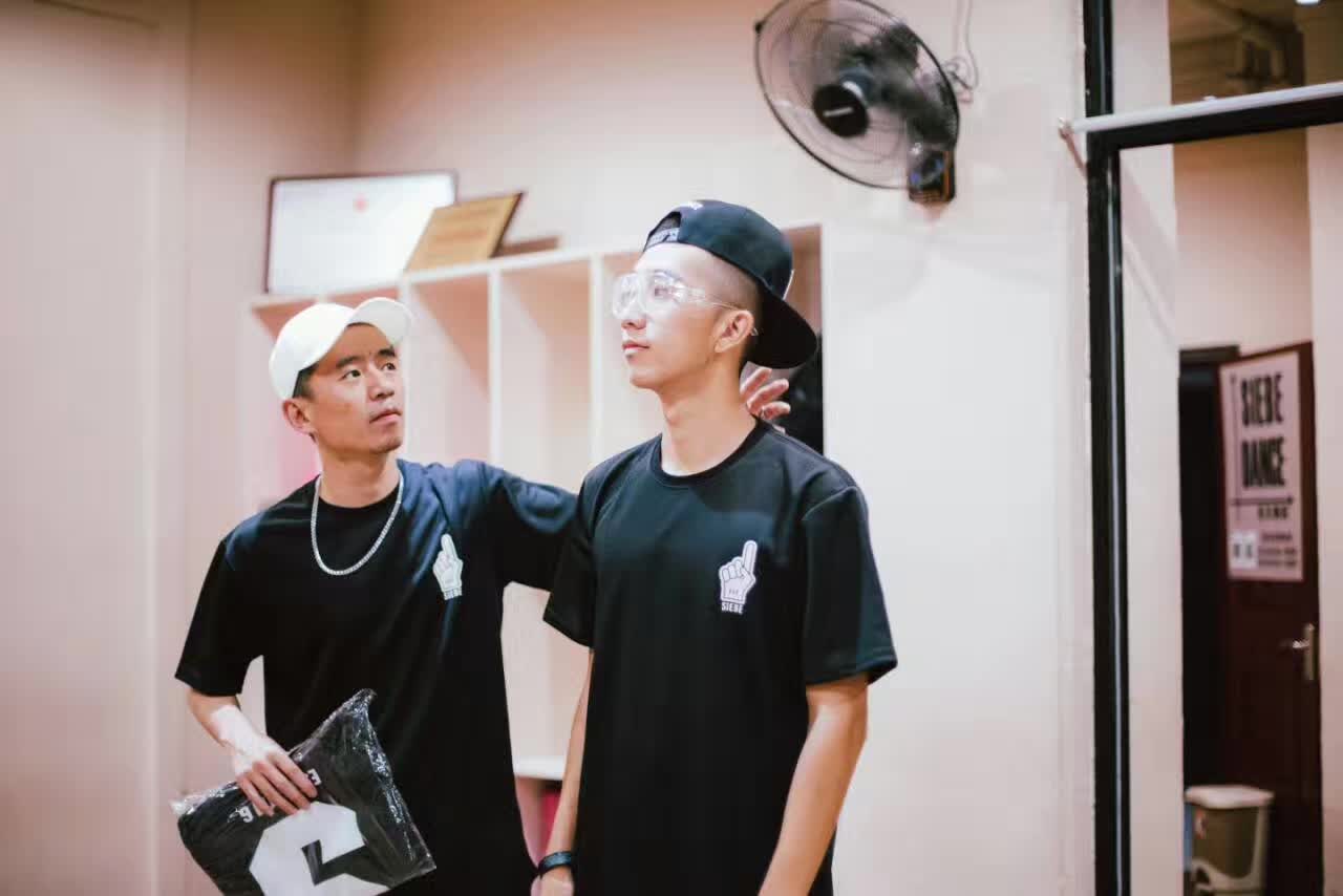 Two people wearing black T-shirts and caps posing together indoors.