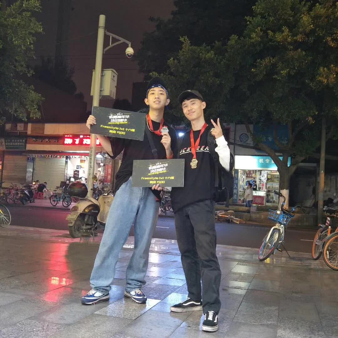 Two dancers wearing medals and holding competition certificates outdoors at night.