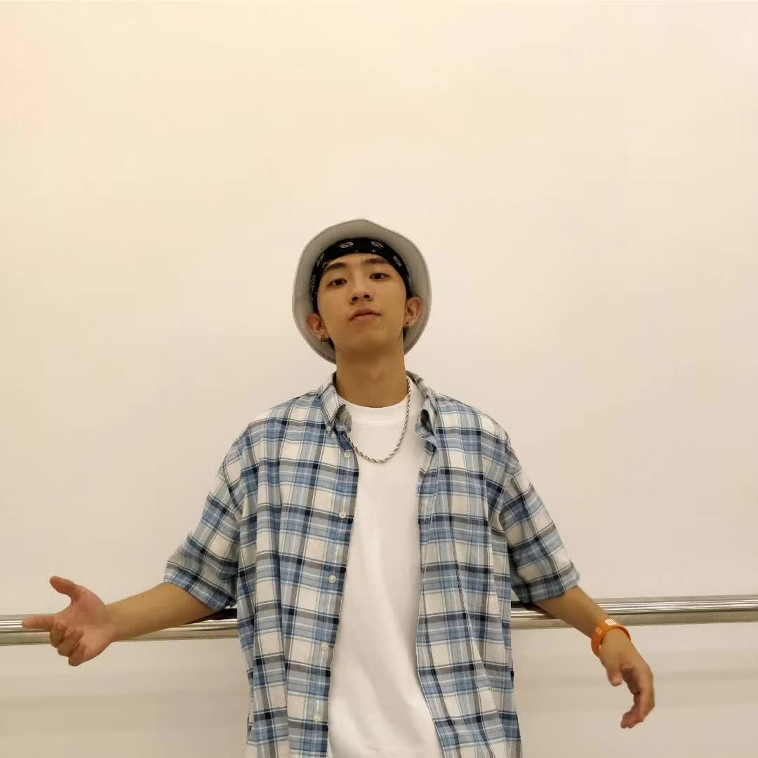 A person wearing a bucket hat and a plaid shirt posing in a dance studio.