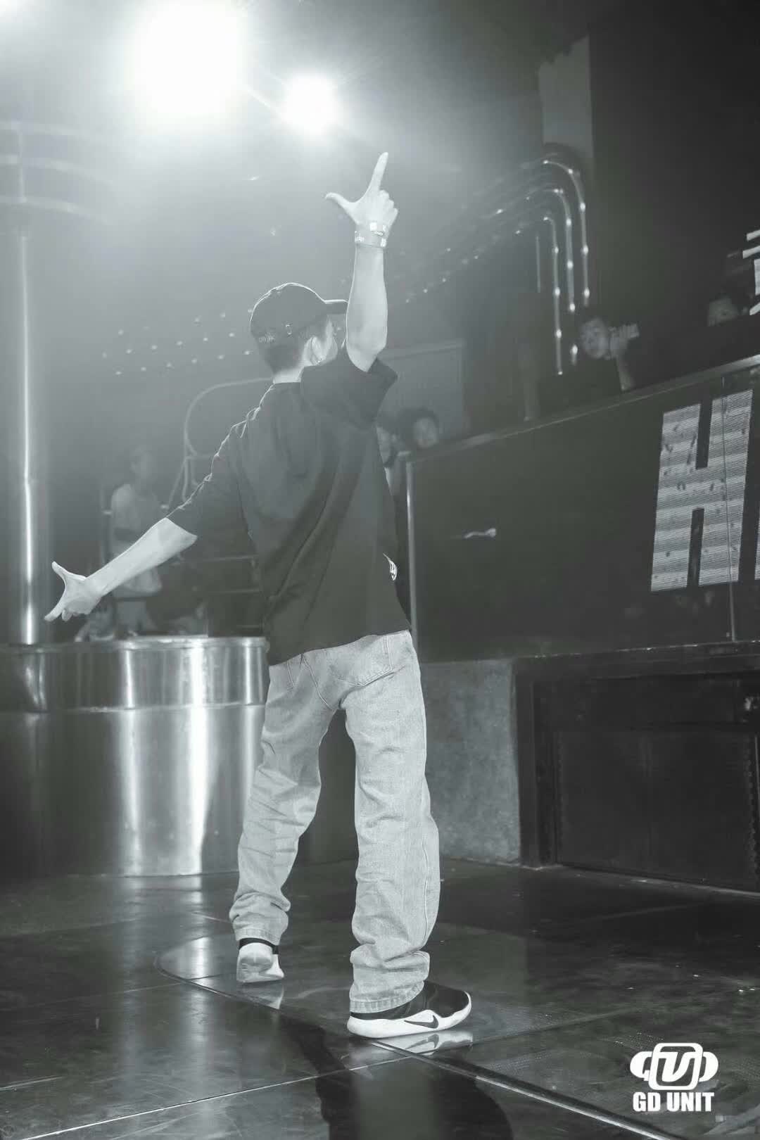 A black-and-white photograph of a dancer performing on stage with one arm raised.