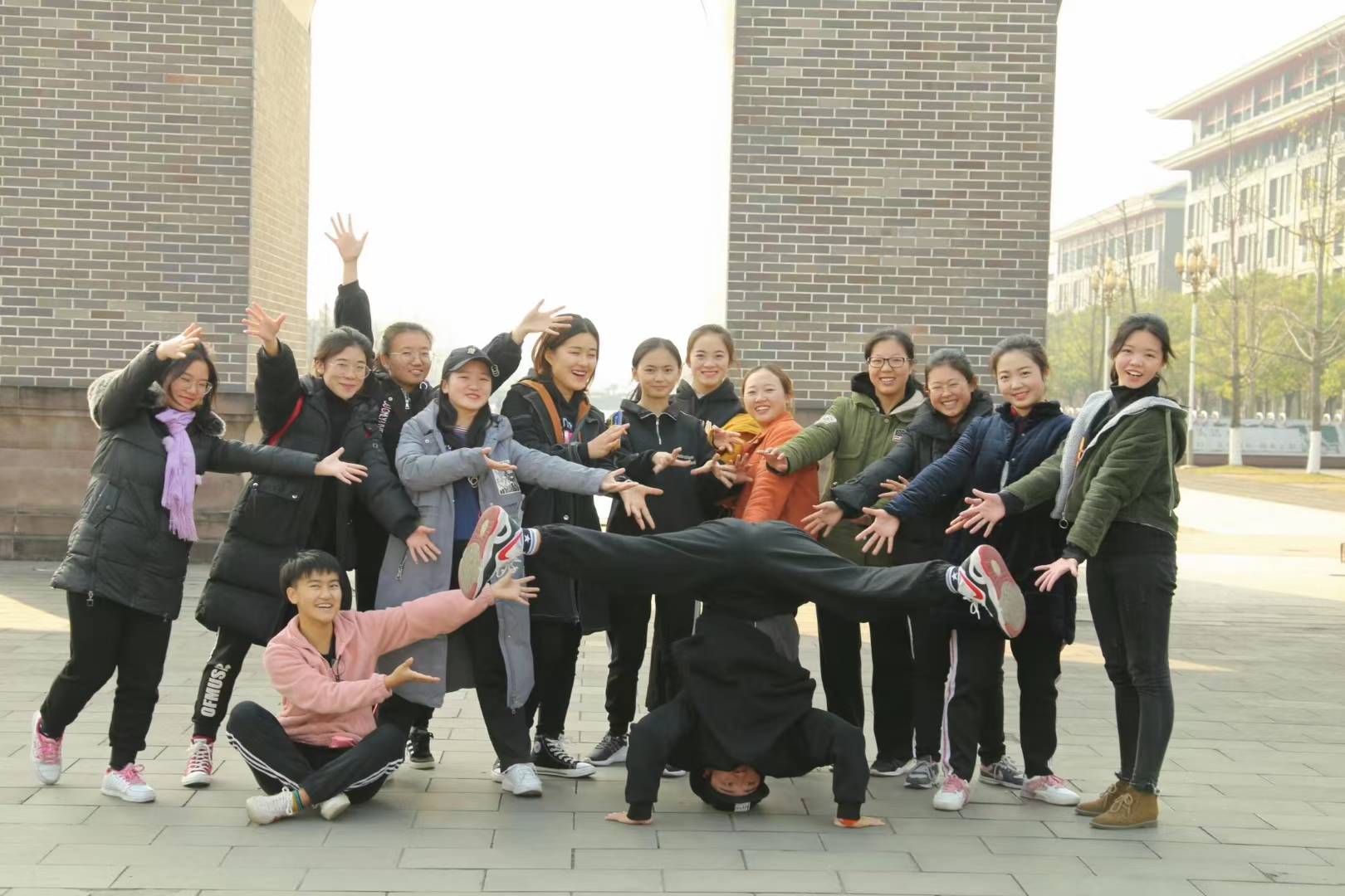 A dance class posing outdoors around a dancer performing a headstand.