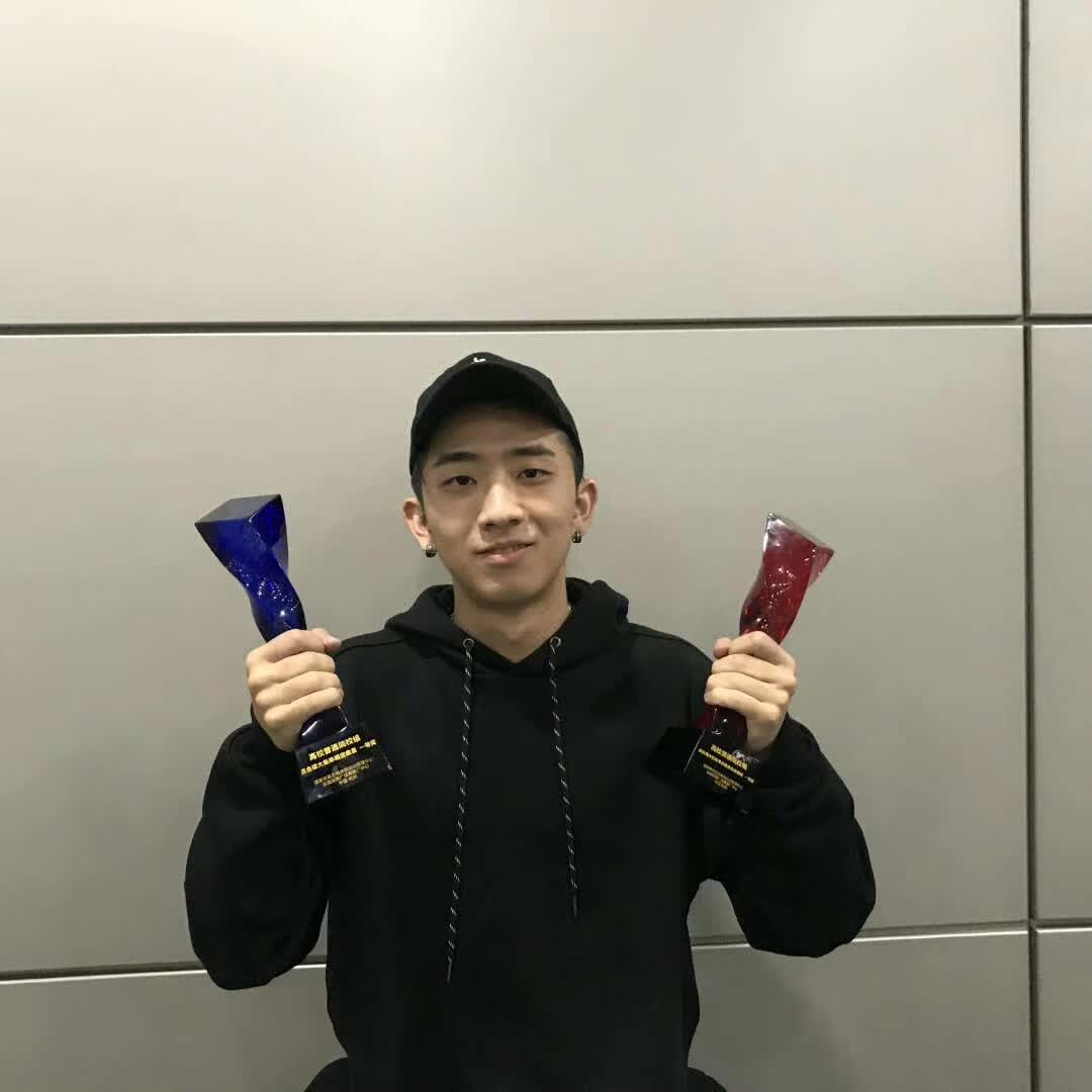 Holding two championship trophies while wearing a black hoodie and cap.