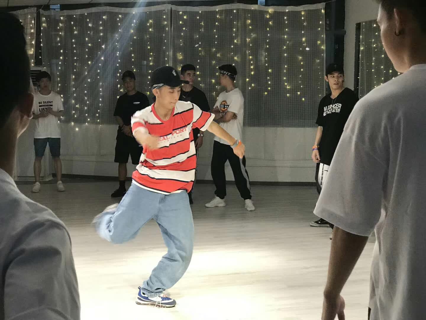 A dancer in a red striped shirt performing in a studio surrounded by other dancers.