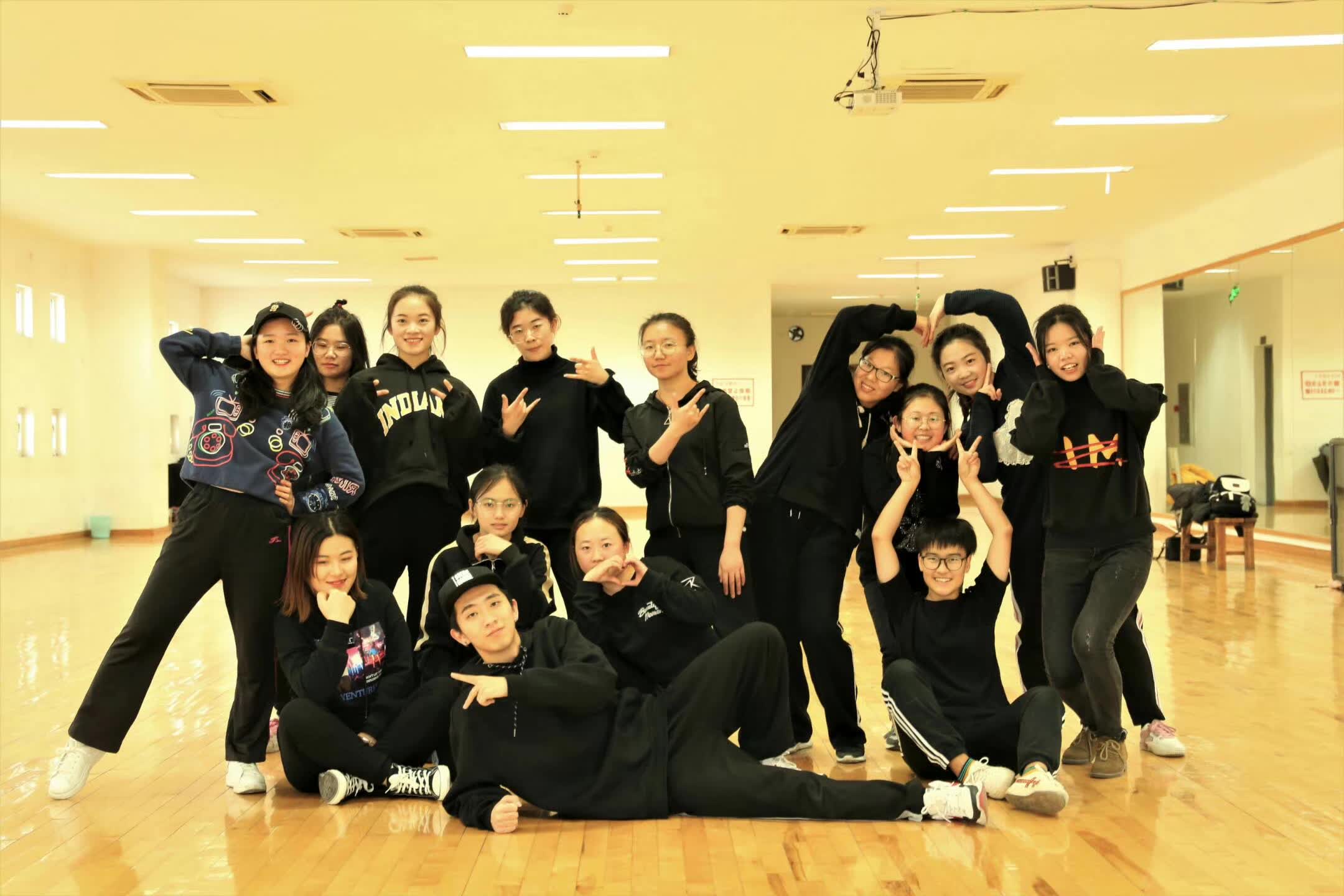 A street dance class posing together in a bright mirrored dance studio.