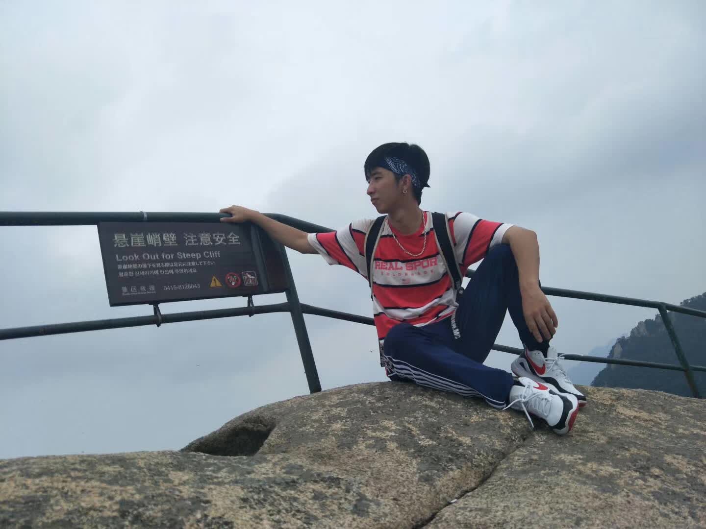 Sitting on a rock beside a railing at a misty mountain viewpoint.