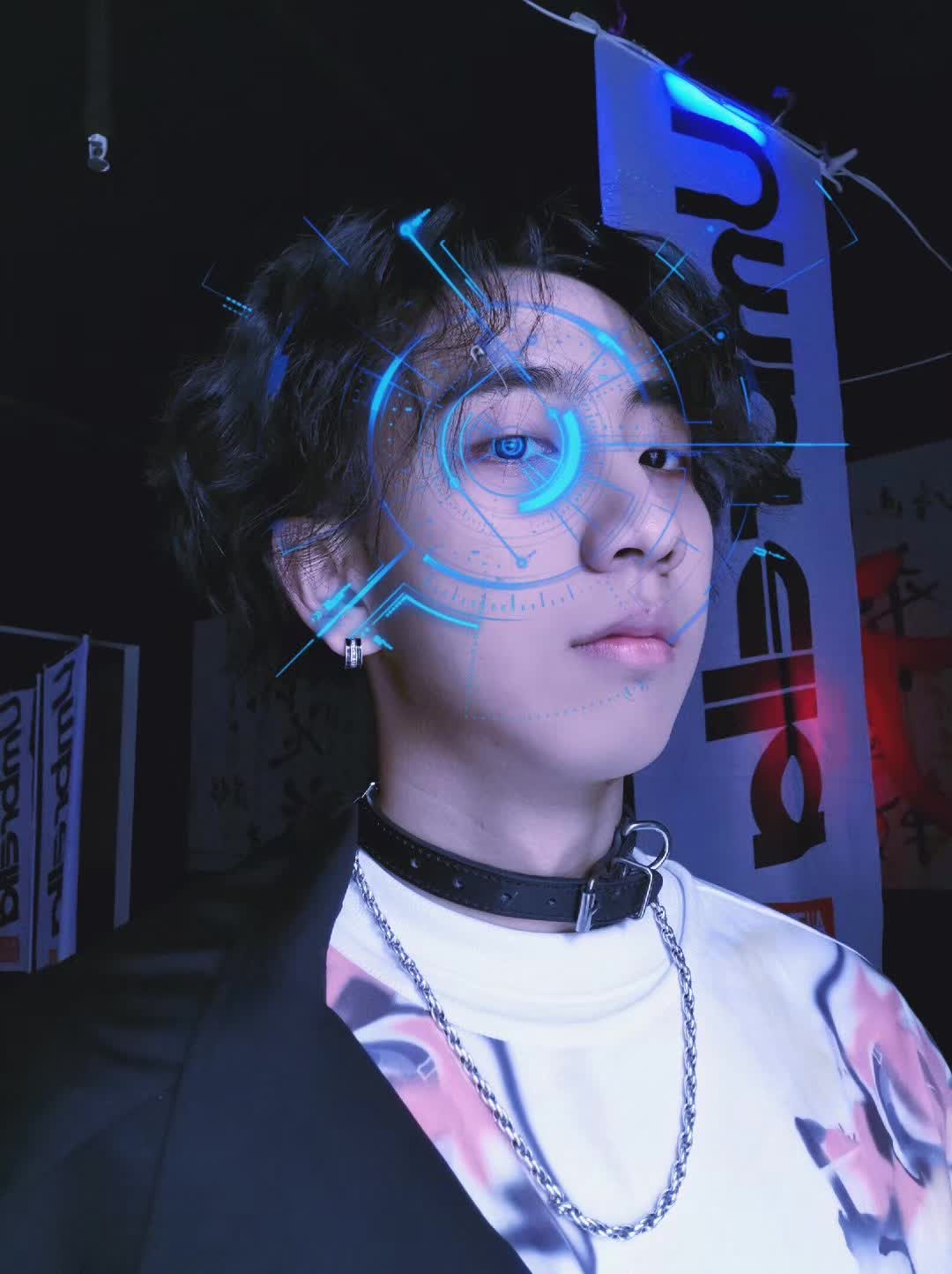 A portrait with blue futuristic graphics over one eye and a silver chain necklace.