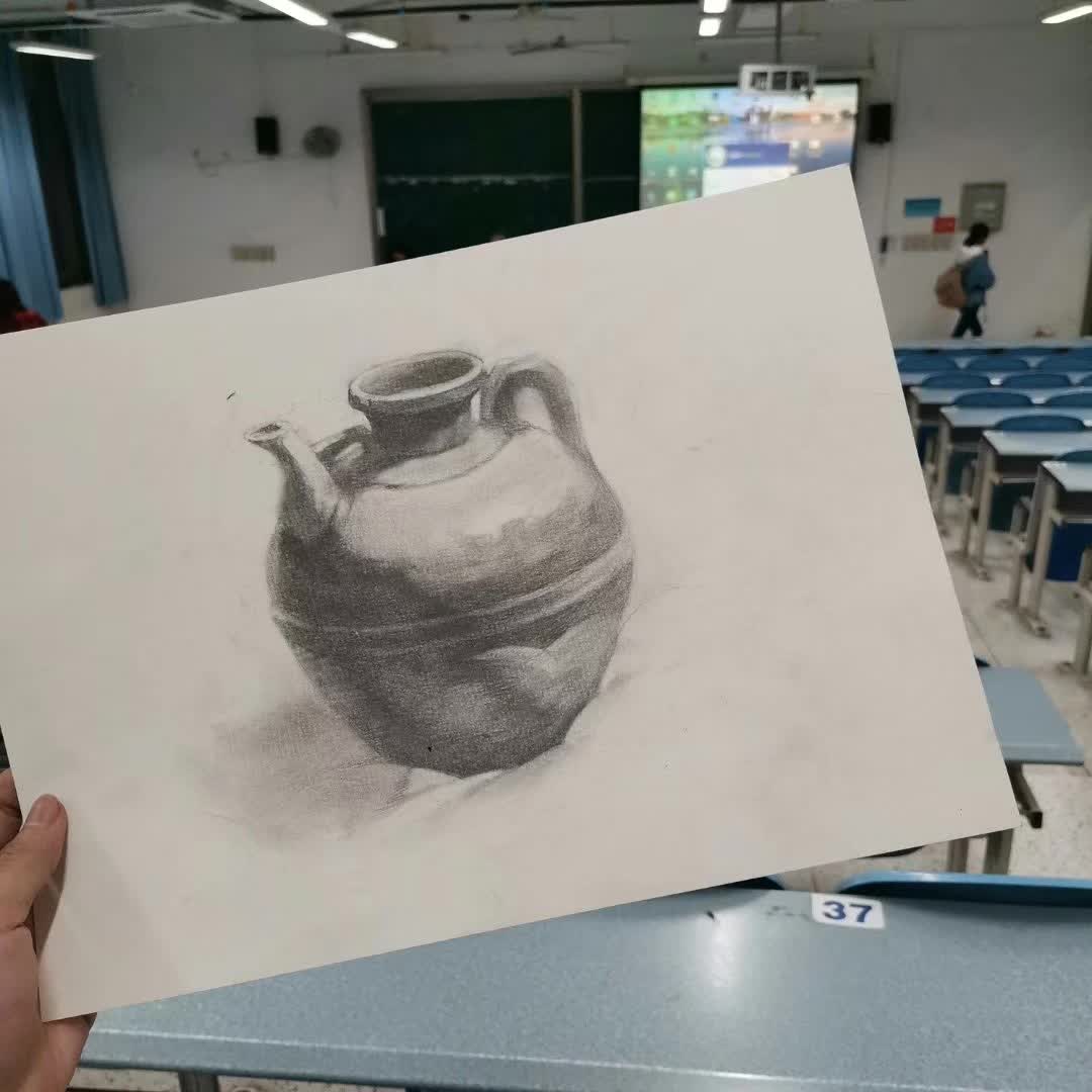 A hand holding a shaded sketch of a jug in a classroom.