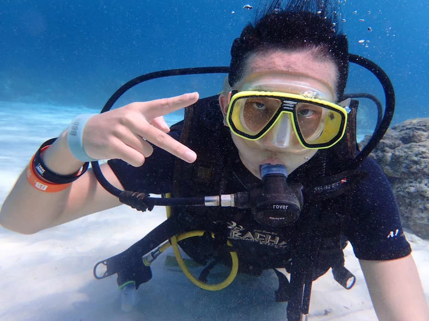 A scuba diver with a yellow mask making a peace sign underwater.