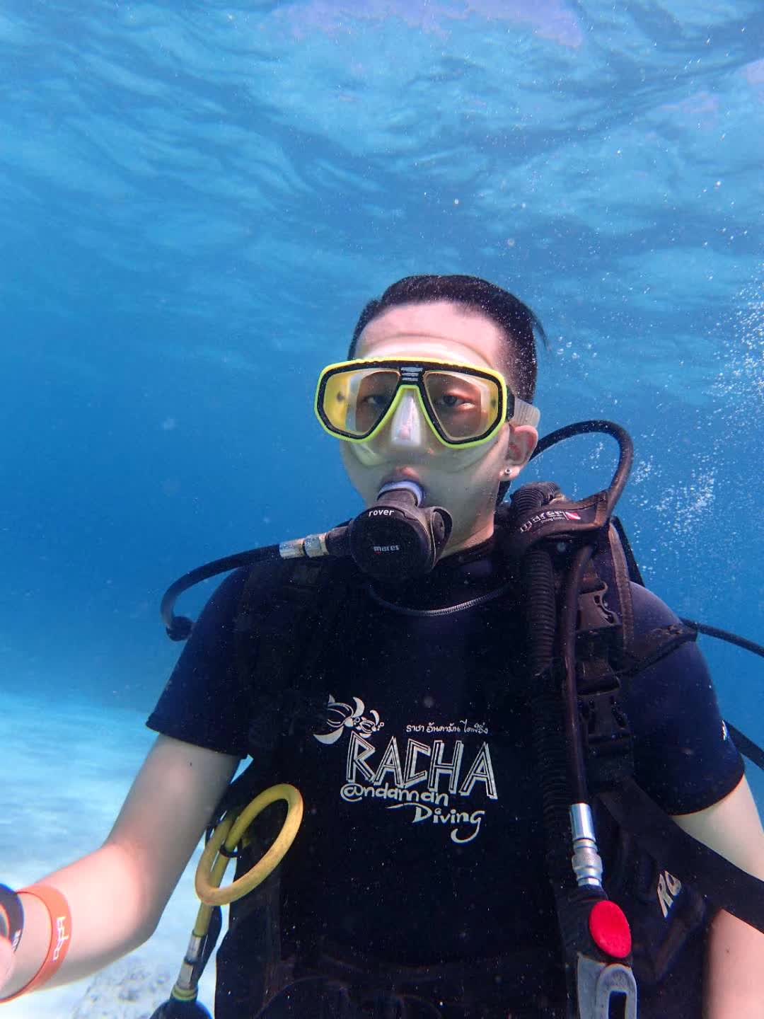 An underwater portrait of a scuba diver wearing a yellow mask and black diving equipment.