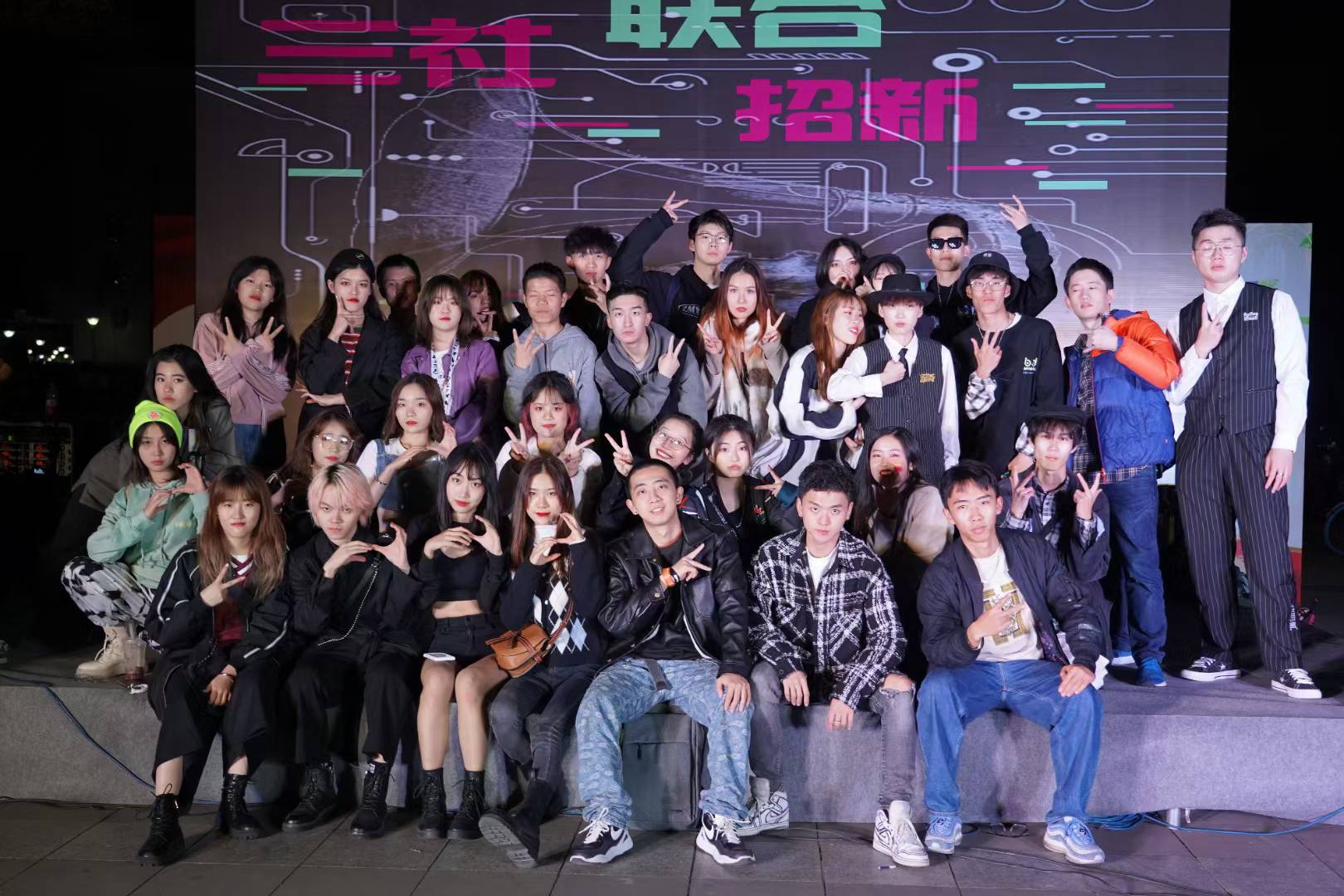 A large group posing on stage in front of a club recruitment backdrop.