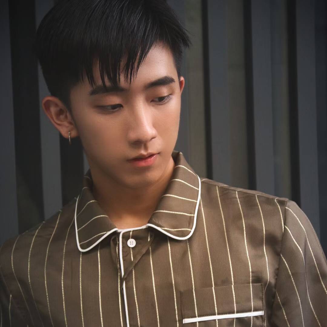 A portrait wearing a brown striped shirt against a dark paneled background.