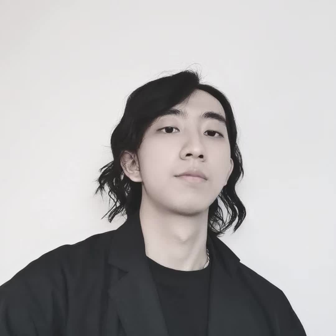 A portrait with wavy hair and a black blazer against a light wall.