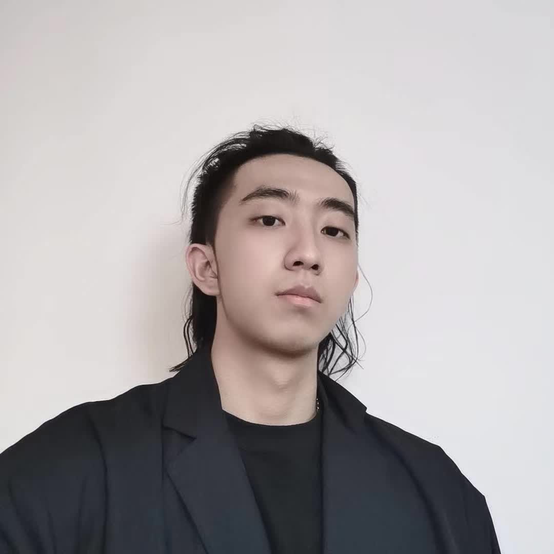 A portrait with swept-back hair and a black blazer against a light wall.