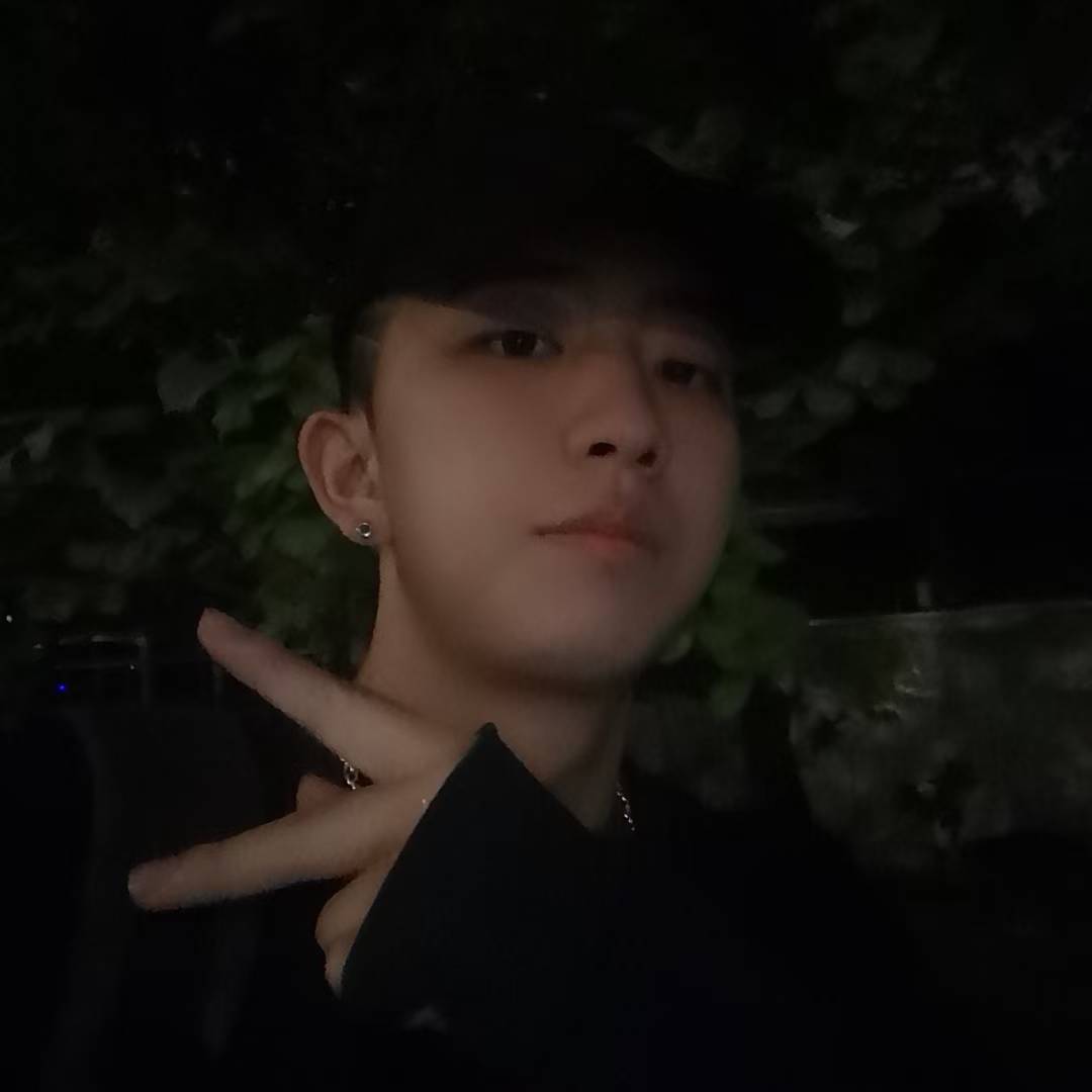 A portrait wearing a black cap and making a peace sign in dim lighting.