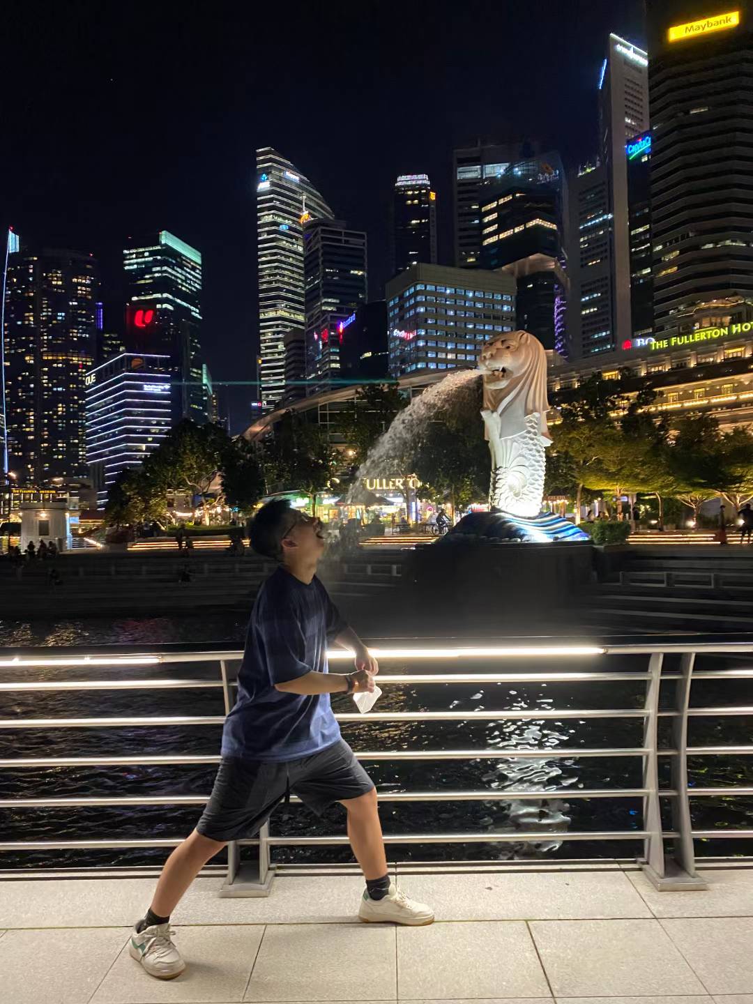Posing beside the waterfront at night with the Merlion and illuminated skyscrapers behind.