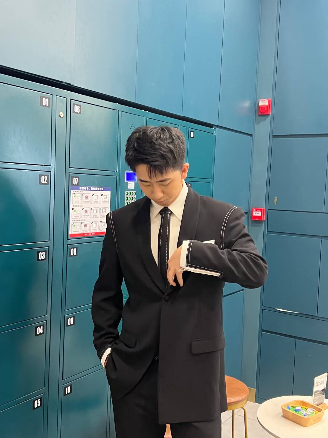 A portrait in a black suit and tie standing beside teal lockers.