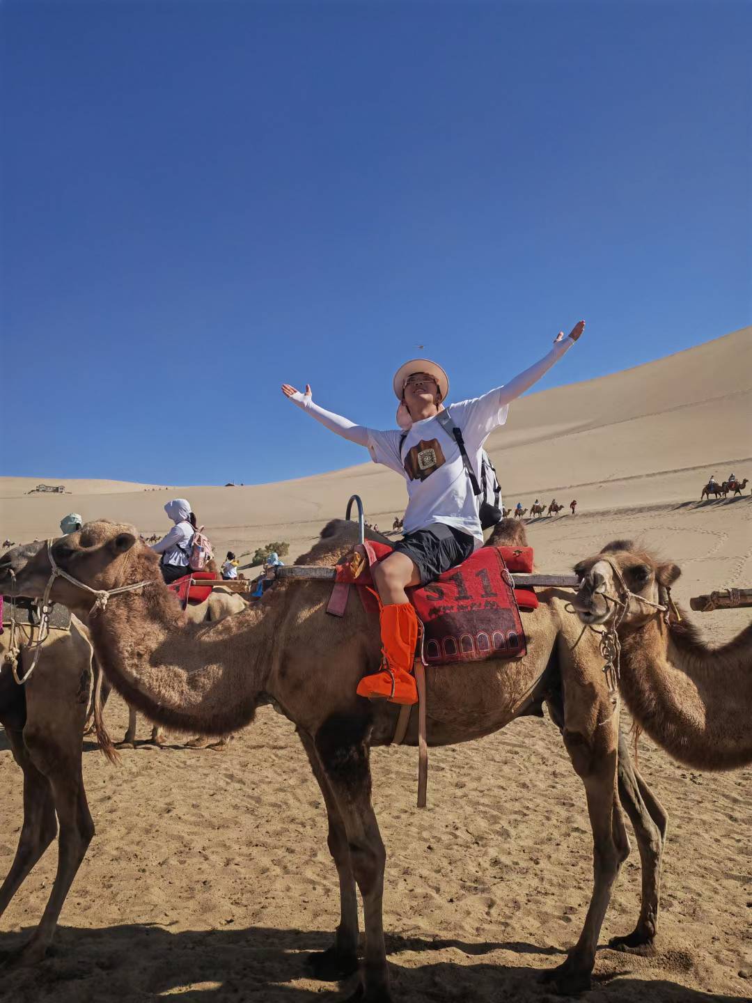 A rider with outstretched arms sitting on a camel among desert dunes under a clear blue sky.