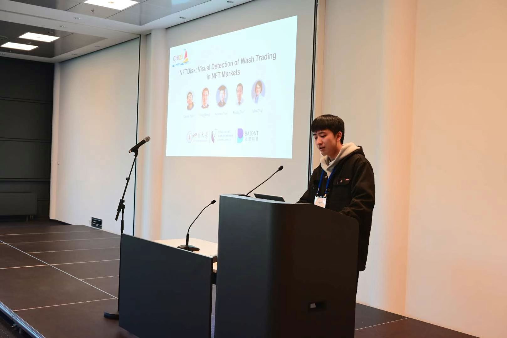 A presenter standing at a lectern with a research presentation projected behind.