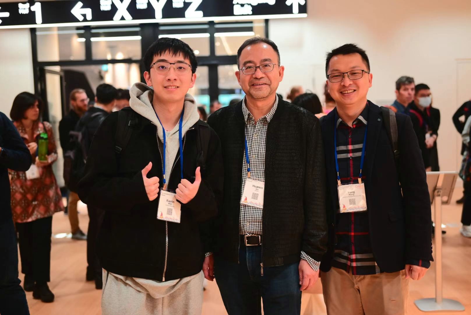 Three attendees wearing conference badges posing together in a busy conference venue.