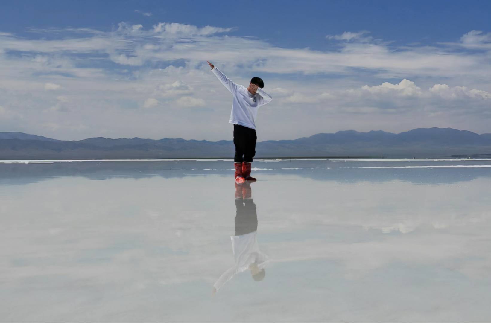 A person posing on a reflective salt lake beneath a blue sky, with mountains in the distance.