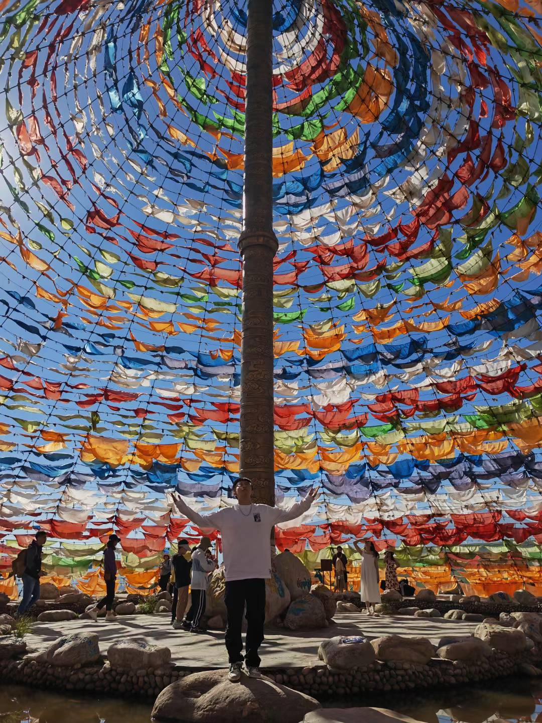 A person standing on a rock beneath a canopy of colorful prayer flags.