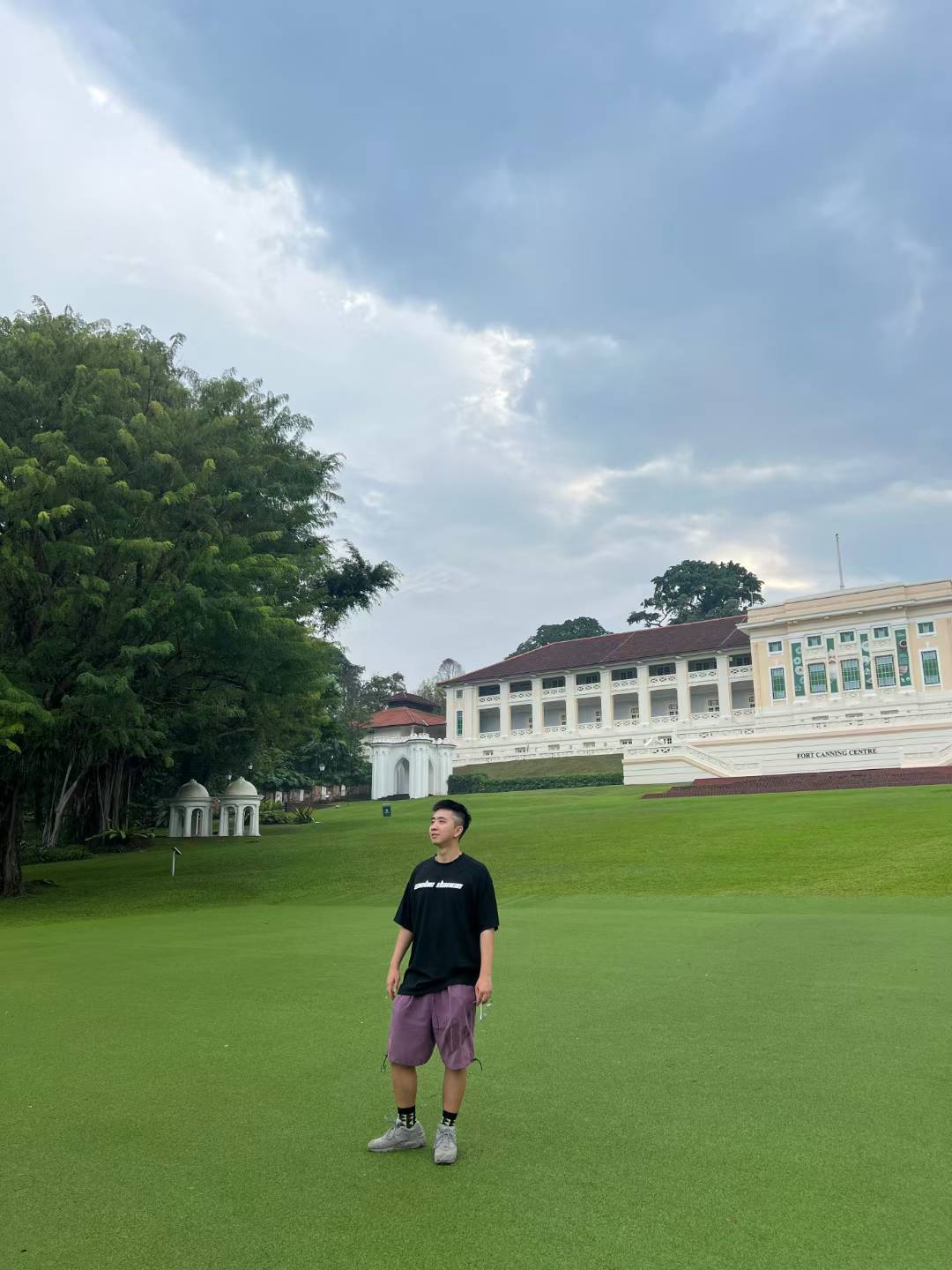 A person standing on the green lawn in front of Fort Canning Centre beneath a cloudy sky.