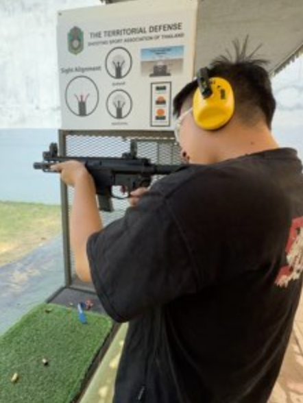 A person wearing yellow hearing protection and holding a firearm at a shooting range.