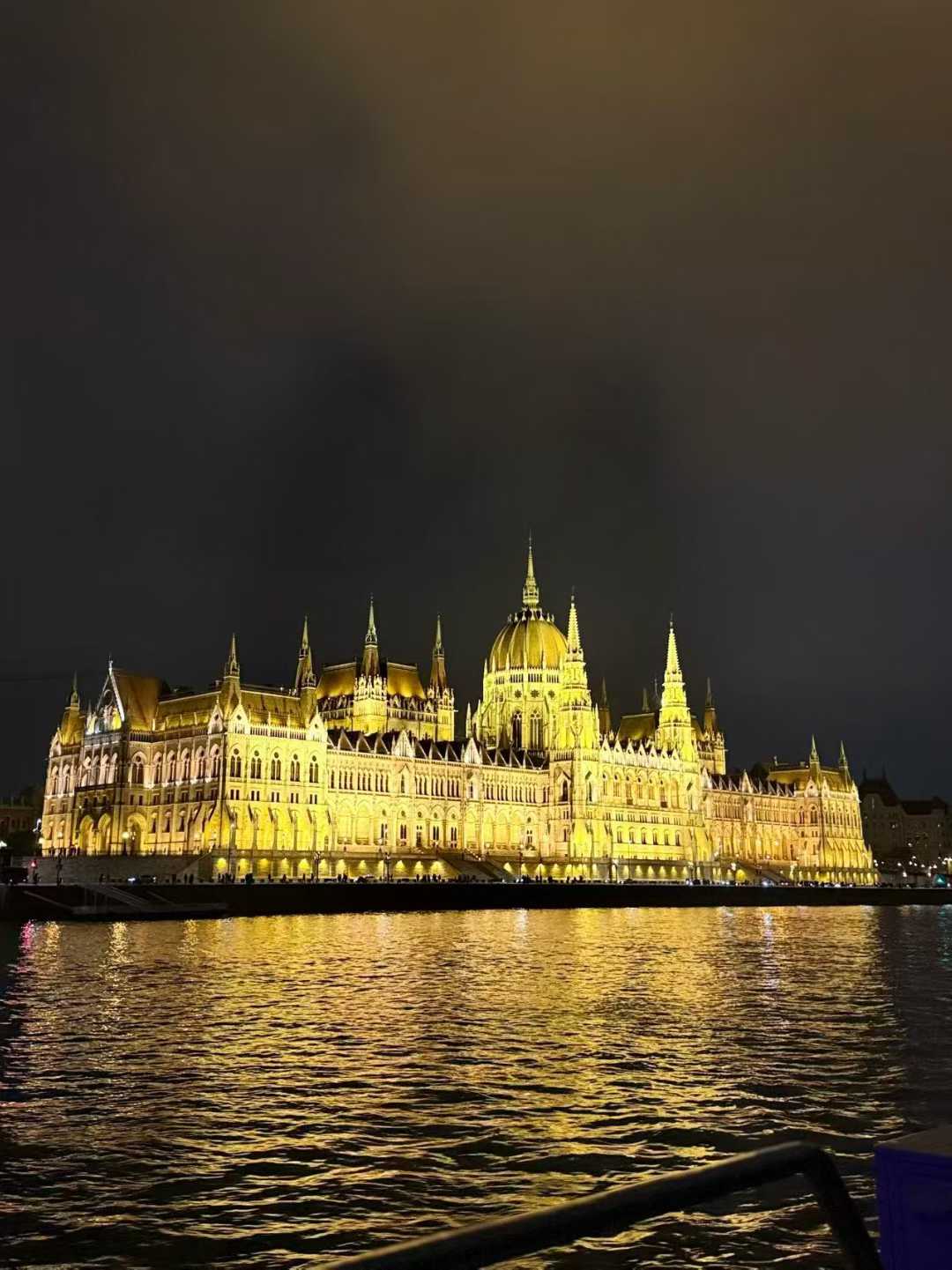 The illuminated Hungarian Parliament Building at night with golden reflections on the river.