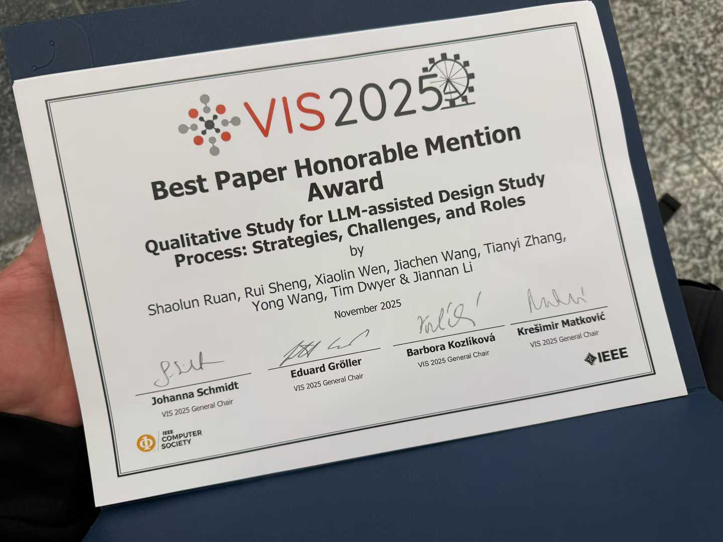 An IEEE VIS 2025 Best Paper Honorable Mention Award certificate in a blue folder.