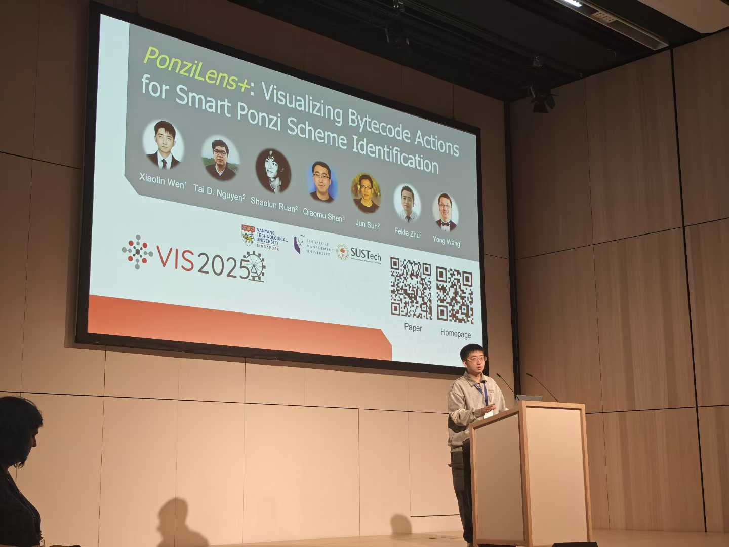 A presenter speaking at a lectern beneath the PonziLens+ title slide at IEEE VIS 2025.