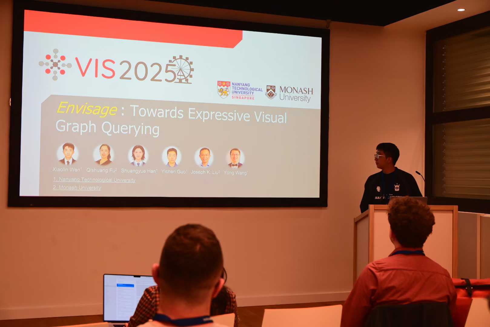 A presenter at a lectern beside the Envisage title slide at IEEE VIS 2025.