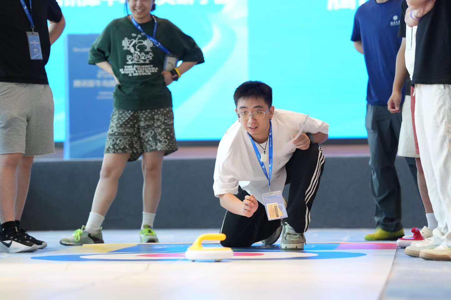 A participant crouching to slide a floor curling stone while other participants watch.